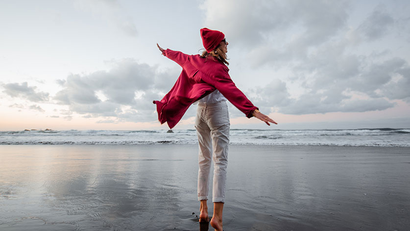 Frau in roter Kleidung fühlt sich lebendig und genießt das Meer und den Strand